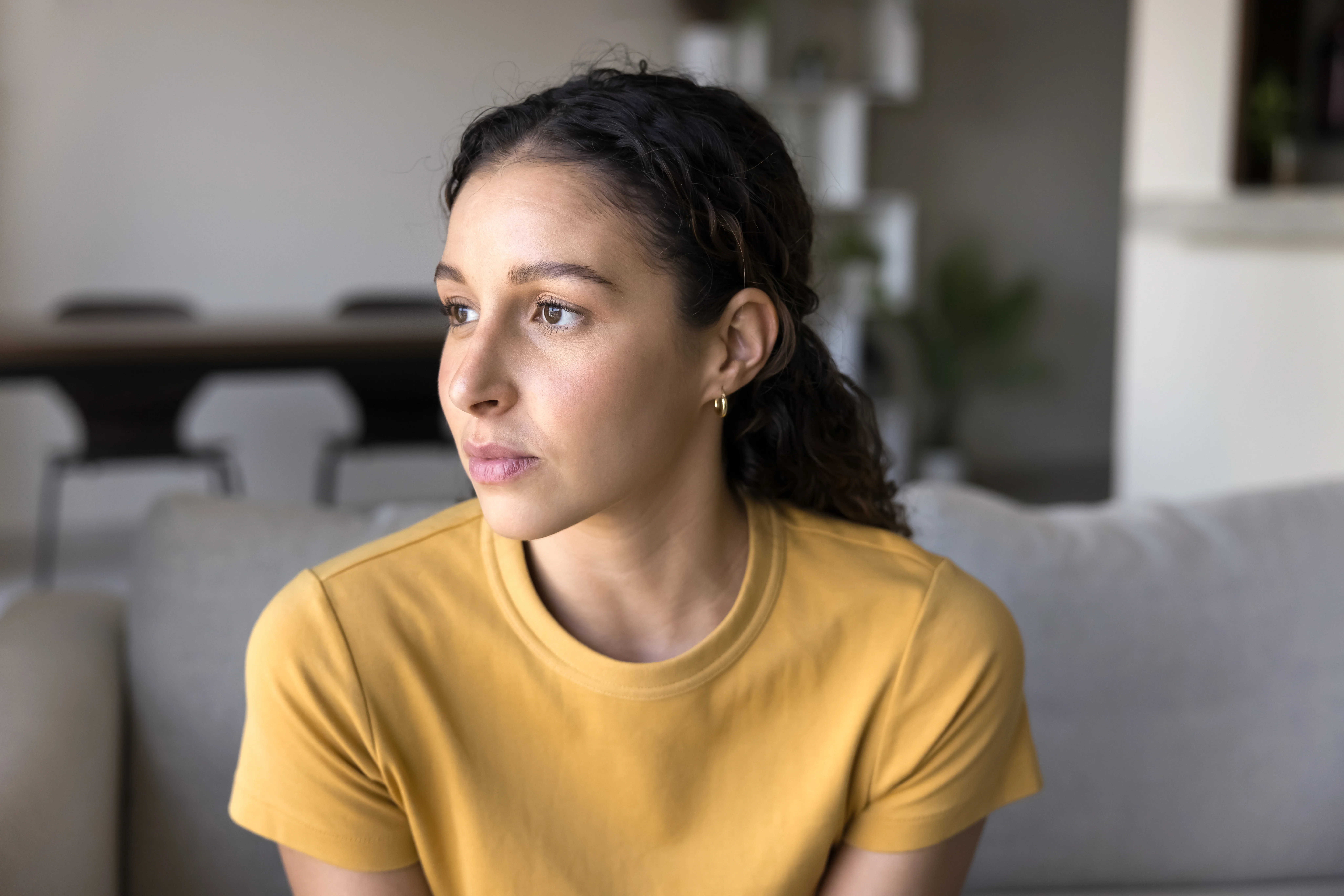 Young woman sitting at home with a thoughtful expression, struggling with generalized anxiety disorder.