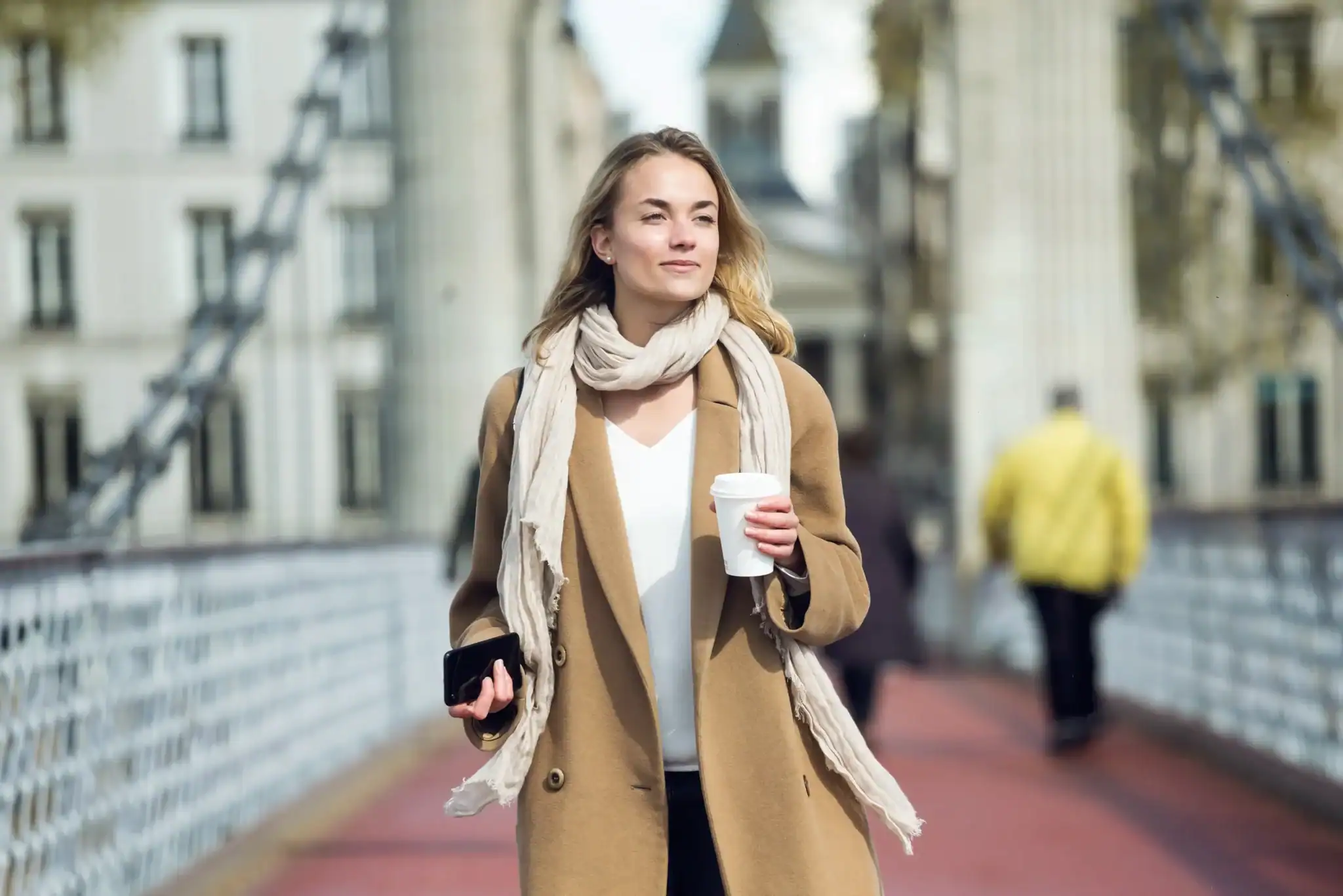Young woman walking through a city holding a coffee, looking ahead calmly