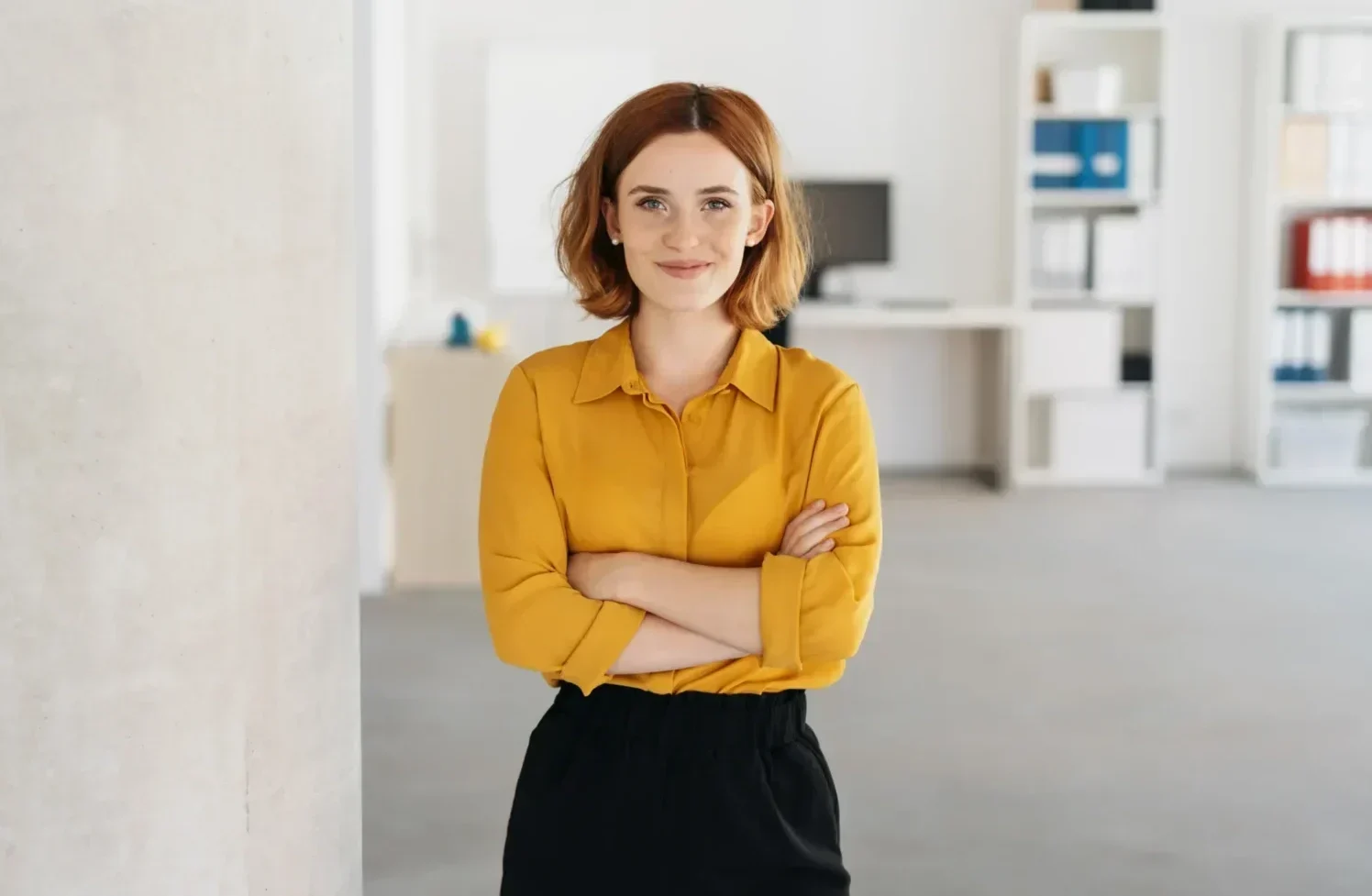 Smiling professional standing with arms crossed in a bright office.