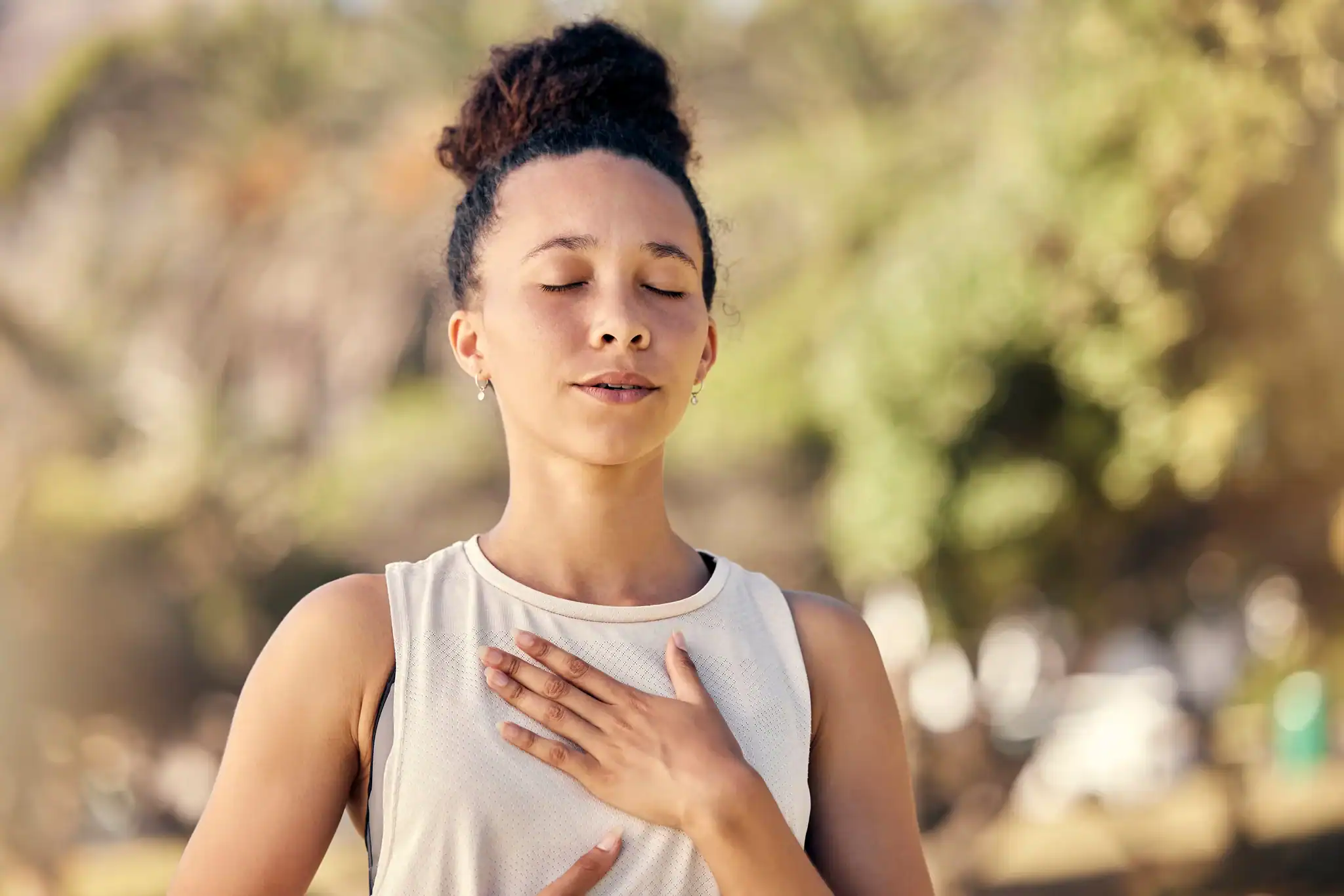 Woman practicing calm breathing outdoors with a hand on her chest to manage anxiety without medication.