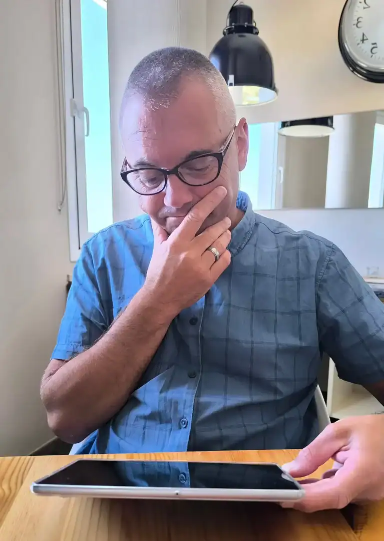 Man sitting at a kitchen table looking thoughtfully at a tablet.