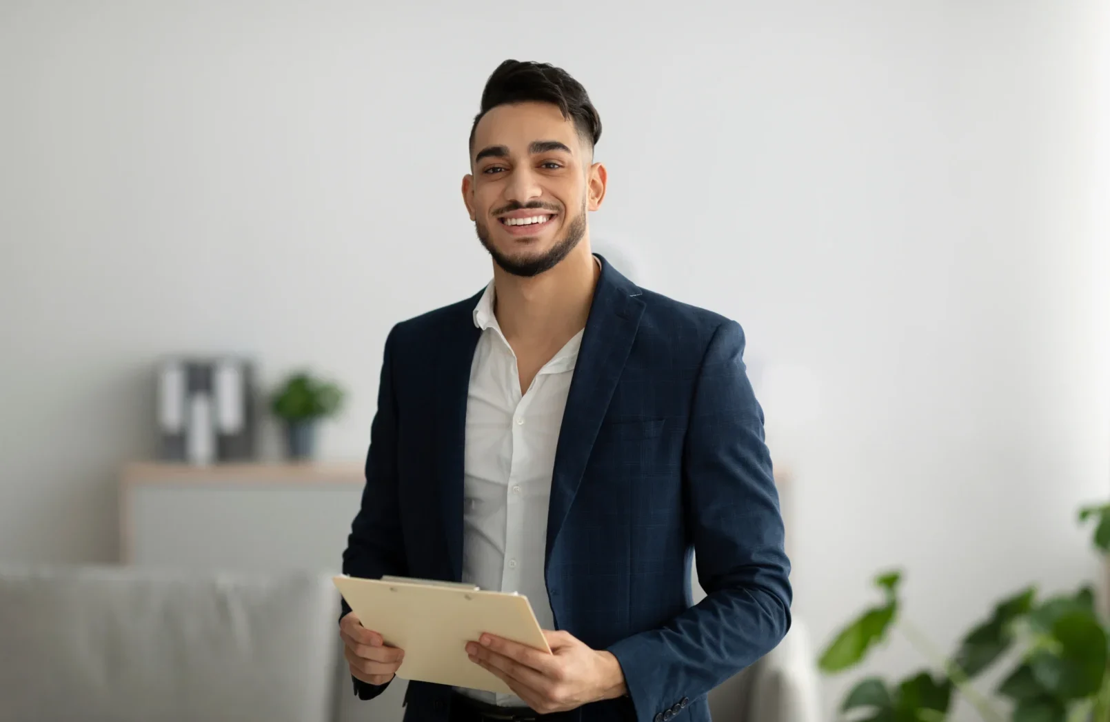 Clinician in a navy blazer holding an assessment clipboard, smiling in a bright office.
