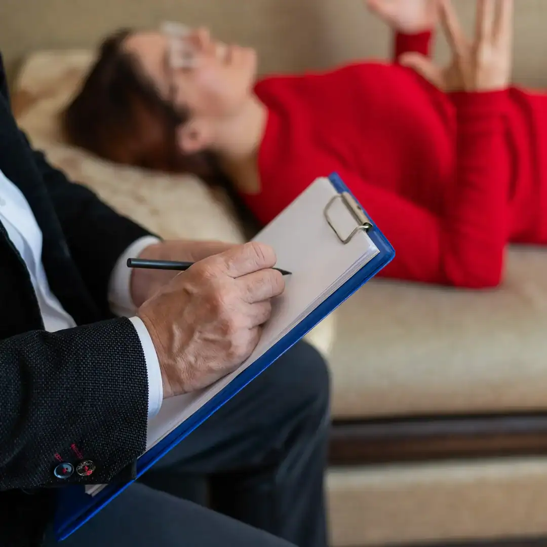 Therapist taking notes on a clipboard while a woman talks during a therapy session.