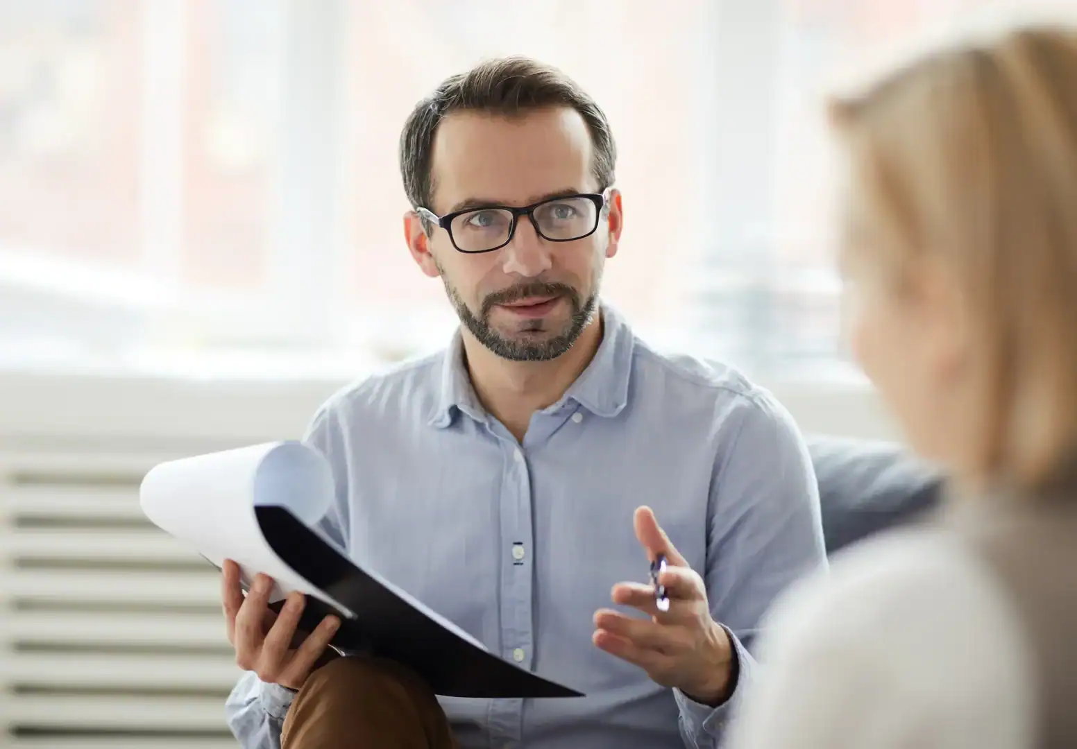 Therapist holding a clipboard while talking with an adult patient during a counseling session.