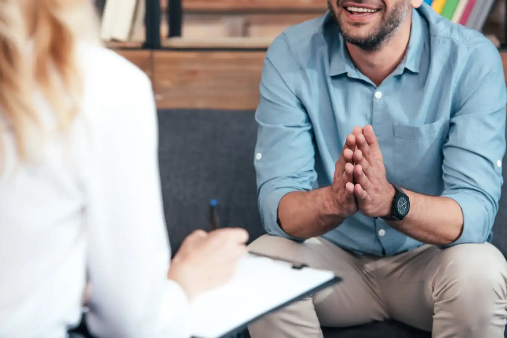 A clinician takes notes on a clipboard during an intake conversation with a smiling adult client.